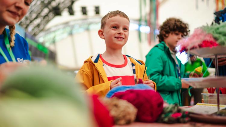 Young boy wearing a white and red t-shirt and yellow rain coat smiling and making crafts with textiles